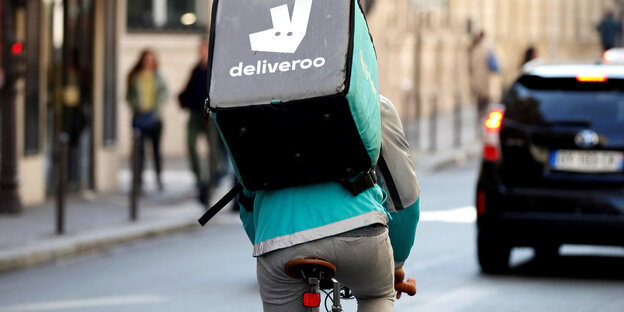 Es scheint. Ein Mensch steht mit einer Deliveroo-Tasche auf der Straße Es scheint. Ein Mensch steht mit einer Deliveroo-Tasche auf der Straße