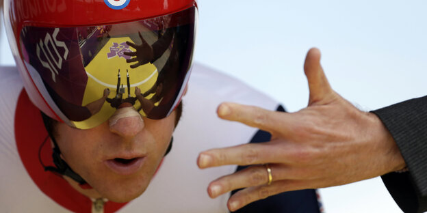 Eine Hand streckt sich in Richtung des Gesichts eines Mannes mit Brille und Helm aus Eine Hand streckt sich in Richtung des Gesichts eines Mannes mit Brille und Helm aus