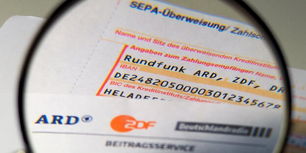 Eine Lupe guckt auf ein Anschreiben zu den Rundfunkgebühren und ein Überweisungsschein für ein Jahr Rundfunkgebühr Eine Lupe guckt auf ein Anschreiben zu den Rundfunkgebühren und ein Überweisungsschein für ein Jahr Rundfunkgebühr