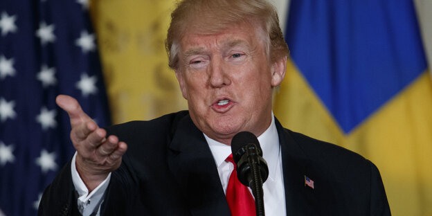 Donald Trump streckt die Hand aus, während er in ein Mikro spricht Donald Trump streckt die Hand aus, während er in ein Mikro spricht