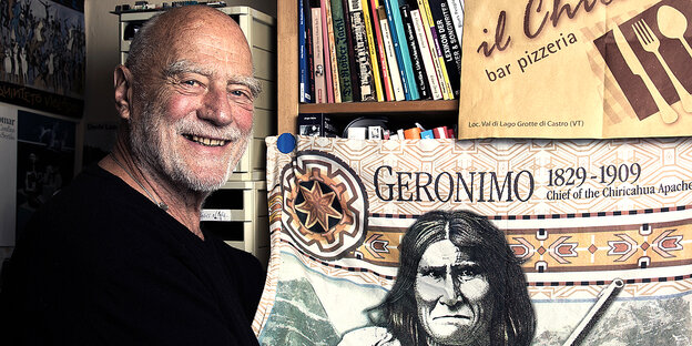 Achim Bergmann vor Bücherregal und Geronimo-Fahne Achim Bergmann vor Bücherregal und Geronimo-Fahne