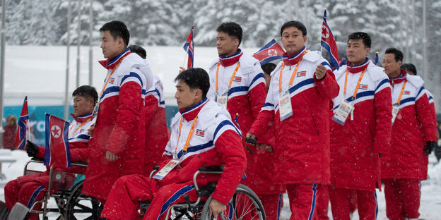 Mehrere Sportler in einheitlichen Trainingsbekleidung im Schnee, darunter auch Rollstuhlfahrer Mehrere Sportler in einheitlichen Trainingsbekleidung im Schnee, darunter auch Rollstuhlfahrer