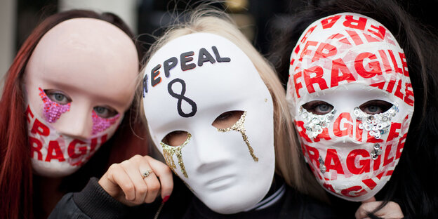 Drei Menschen tragen Masken im Gesicht, auf denen „Fragile“ und „Repeal“ steht Drei Menschen tragen Masken im Gesicht, auf denen „Fragile“ und „Repeal“ steht