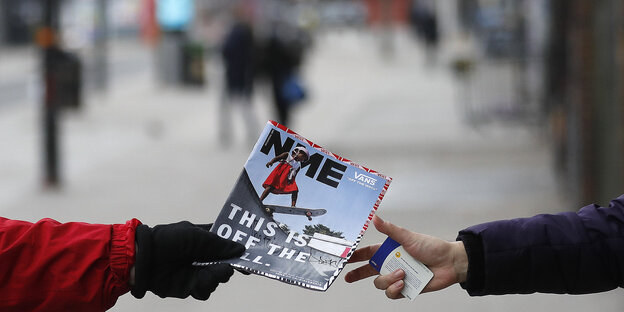 Eine NME-Ausgabe wird von zwei ausgestreckten Händen gehalten - im Hintergrund eine Straßenszenerie Eine NME-Ausgabe wird von zwei ausgestreckten Händen gehalten - im Hintergrund eine Straßenszenerie