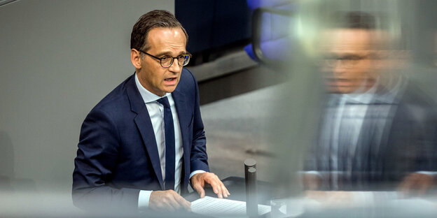 Heiko Maas spricht im Bundestag und spiegelt sich in einer Scheibe