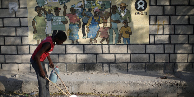 Ein Junge spielt in einem Flüchtlngscamp auf Haiti vor einer Wand, auf der das Oxfam-Logo aufgemalt ist Ein Junge spielt in einem Flüchtlngscamp auf Haiti vor einer Wand, auf der das Oxfam-Logo aufgemalt ist