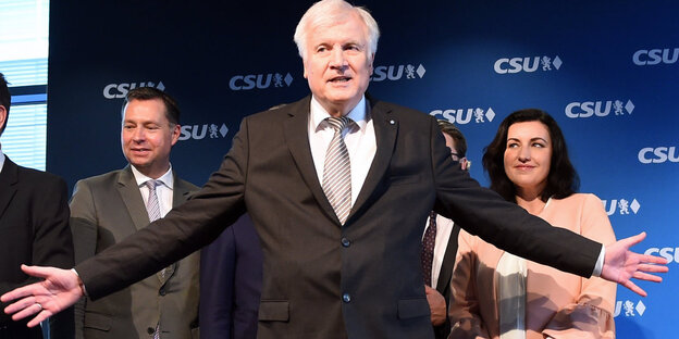 Ein Mann, Horst Seehofer, streckt die Arme weit zu beiden Seiten aus, im Hintergrund stehen mehrere Menschen, gut sichtbar ist ein Mann zu seiner linken und seine Frau zu seiner rechten, die ihn anschaut Ein Mann, Horst Seehofer, streckt die Arme weit zu beiden Seiten aus, im Hintergrund stehen mehrere Menschen, gut sichtbar ist ein Mann zu seiner linken und seine Frau zu seiner rechten, die ihn anschaut