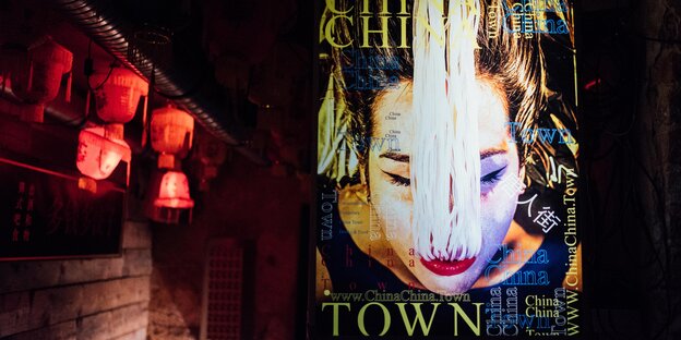 Screen mit chinesischer Frau, der Nudeln aus dem Mund hängen. Daneben rote Lampions. Screen mit chinesischer Frau, der Nudeln aus dem Mund hängen. Daneben rote Lampions.
