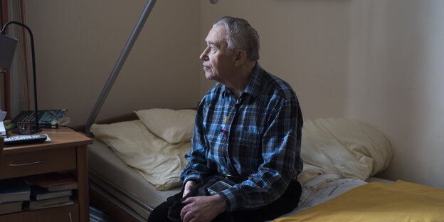 Ein älterer Mann sitzt auf seinem Bett Ein älterer Mann sitzt auf seinem Bett