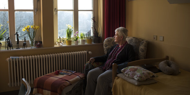 Eine ältere Frau sitzt auf einem Sessel und schaut aus dem Fenster Eine ältere Frau sitzt auf einem Sessel und schaut aus dem Fenster