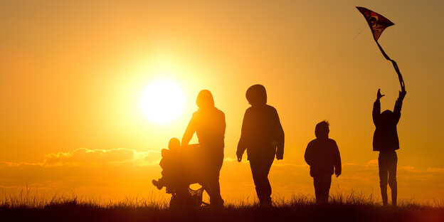 Eine Familie mit Kinderwagen und einem Drachen an der Schnur geht bei Sonnenuntergang über einen Weg durch die Salzwiesen im Watt bei Westerhever Eine Familie mit Kinderwagen und einem Drachen an der Schnur geht bei Sonnenuntergang über einen Weg durch die Salzwiesen im Watt bei Westerhever