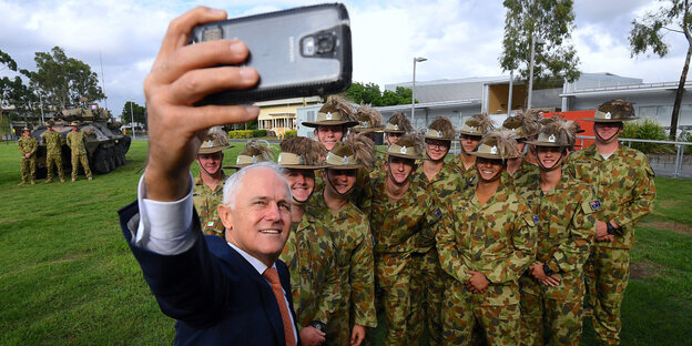 Ein Mann in Anzug macht ein Selfie von sich und einer Gruppe uniformierter Soldaten Ein Mann in Anzug macht ein Selfie von sich und einer Gruppe uniformierter Soldaten
