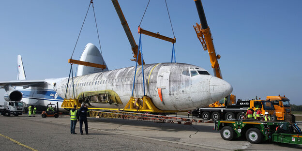 Ein Kran hebt ein altes Flugzeug auf ein Fahrzeug Ein Kran hebt ein altes Flugzeug auf ein Fahrzeug