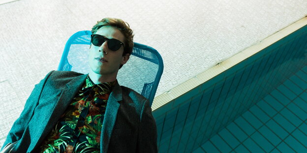 Ein Mann mit Sonnenbrille auf der Nase liegt an einem Pool auf einem Liegestuhl Ein Mann mit Sonnenbrille auf der Nase liegt an einem Pool auf einem Liegestuhl