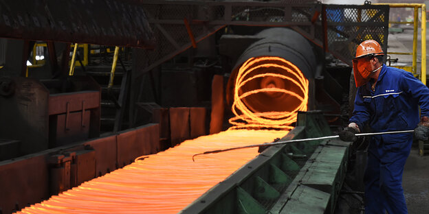 Ein Mann in einem Blaumann arbeitet mit flüssigem Stahl, der orange glüht Ein Mann in einem Blaumann arbeitet mit flüssigem Stahl, der orange glüht