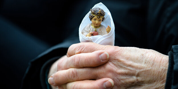 Gefaltete Hände, in denen eine christliche Figur steckt Gefaltete Hände, in denen eine christliche Figur steckt