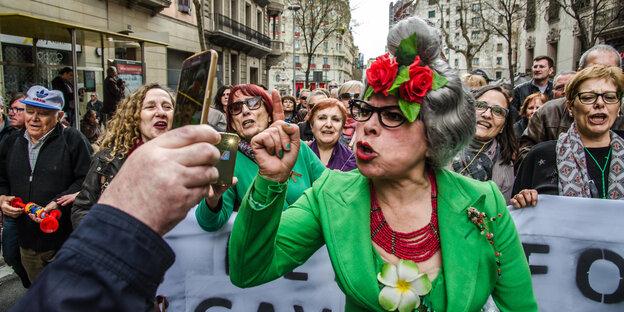 eine Demonstrantin mit erhobenem Zeigefinger blickt in eine Handykamera, im Hintergrund weitere DemonstrantInnen