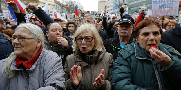 Drei Frauen stehen nebeneinander: Die mittige ruft, die an der rechten Seite bläst in eine Trillerpfeife. Hinter ihnen weitere Demonstranten Drei Frauen stehen nebeneinander: Die mittige ruft, die an der rechten Seite bläst in eine Trillerpfeife. Hinter ihnen weitere Demonstranten
