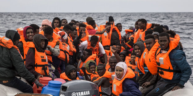 Viele Menschen sitzen in orangen Rettungswesten in einem überfüllten Schlauchboot Viele Menschen sitzen in orangen Rettungswesten in einem überfüllten Schlauchboot