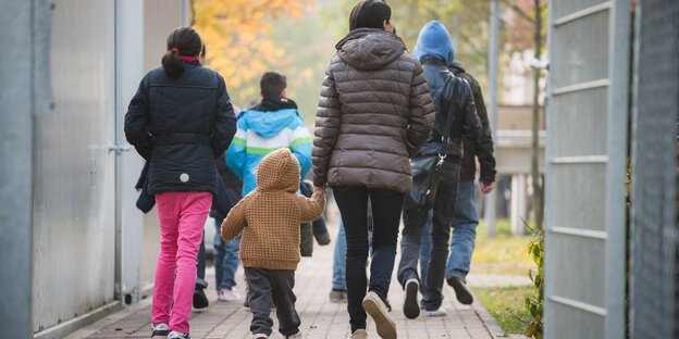 Menschen laufen einen vergitterten Weg in einer Rückführungseinrichtung entlang Menschen laufen einen vergitterten Weg in einer Rückführungseinrichtung entlang