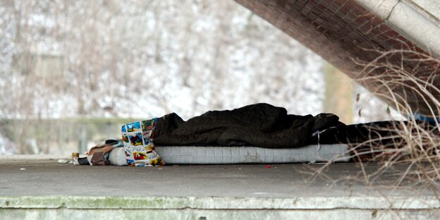 Ein Schlafsack liegt unter einer Brücke auf dem gepflasterten Boden. Ein Schlafsack liegt unter einer Brücke auf dem gepflasterten Boden.