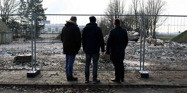 Drei Menschen stehen vor einem Zaun Drei Menschen stehen vor einem Zaun