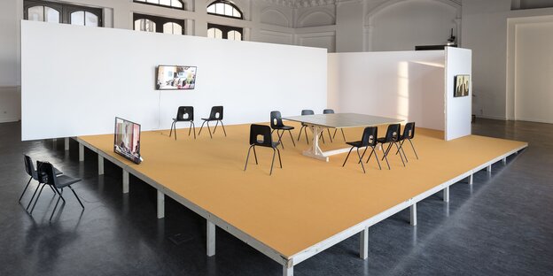 Auf einer niedrigen Bühne stehen ein Tisch mit mehreren Stühlen und ein Fernseher mit zwei Stühlen davor. An der Wand hängt ein Fernseher, ebenfalls mit Stühlen davor. Auf einer niedrigen Bühne stehen ein Tisch mit mehreren Stühlen und ein Fernseher mit zwei Stühlen davor. An der Wand hängt ein Fernseher, ebenfalls mit Stühlen davor.