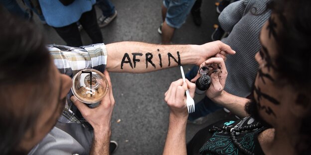 Jemand schreibt "Afrin" auf den Unterarm eines anderen Jemand schreibt "Afrin" auf den Unterarm eines anderen