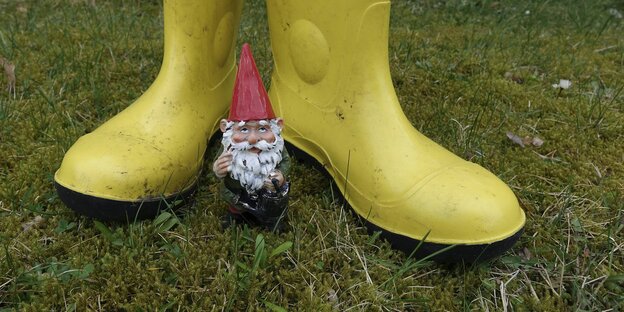 Ein Gartenzwerg steht vor einem Paar Gummistiefel Ein Gartenzwerg steht vor einem Paar Gummistiefel