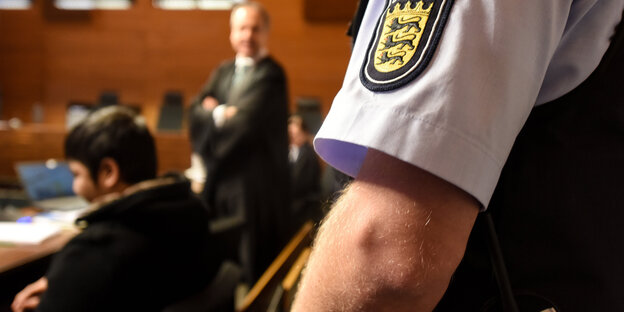 Ein Polizeibeamter steht hinter einem jungen Mann Ein Polizeibeamter steht hinter einem jungen Mann