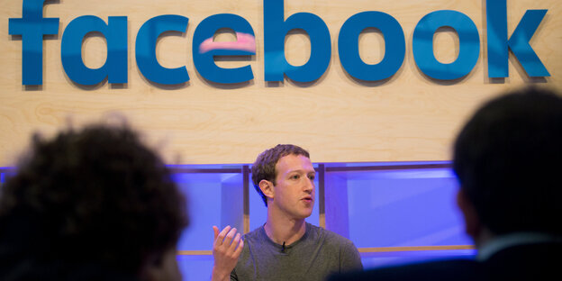Mark Zuckerberg sitzt unter einem Facebooklogo Mark Zuckerberg sitzt unter einem Facebooklogo