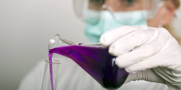 Wissenschaftlerin gießt eine lilafarbene Flüssigkeit aus einem Kolben Wissenschaftlerin gießt eine lilafarbene Flüssigkeit aus einem Kolben