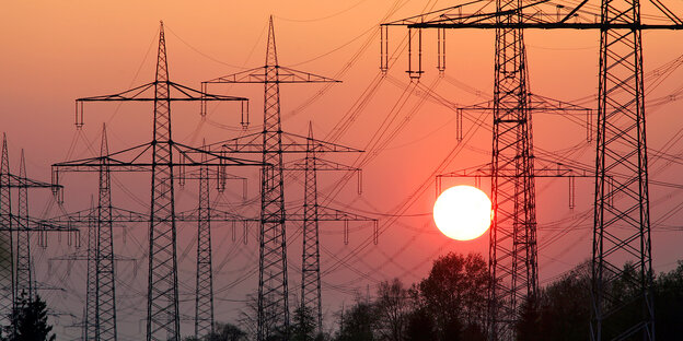 Hinter Hochspannungsmasten geht die Sonne unter