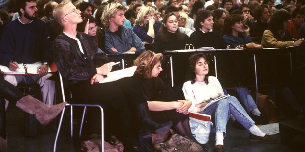 Viele Studierende in einem Hörsaal, ihre Frisuren und Klamotten sehen nach den 80er Jahren aus Viele Studierende in einem Hörsaal, ihre Frisuren und Klamotten sehen nach den 80er Jahren aus