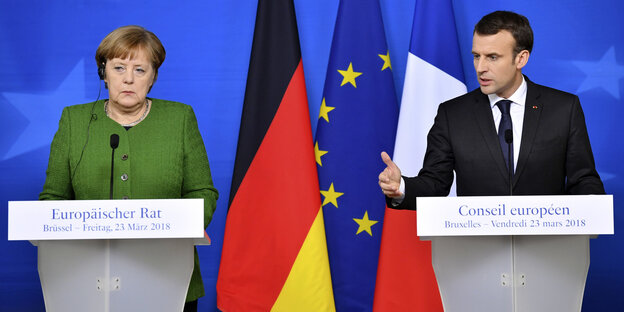 Merkel und Macron stehen nebeneinander an Rednerpulten Merkel und Macron stehen nebeneinander an Rednerpulten