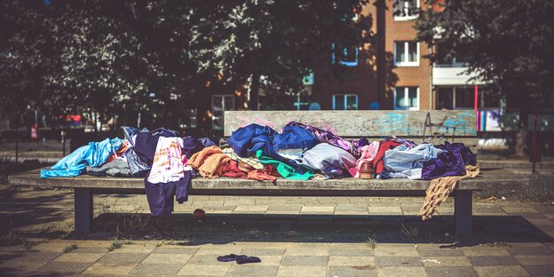 Bunte Kleider sind auf einer Parkbank aufgetürmt Bunte Kleider sind auf einer Parkbank aufgetürmt
