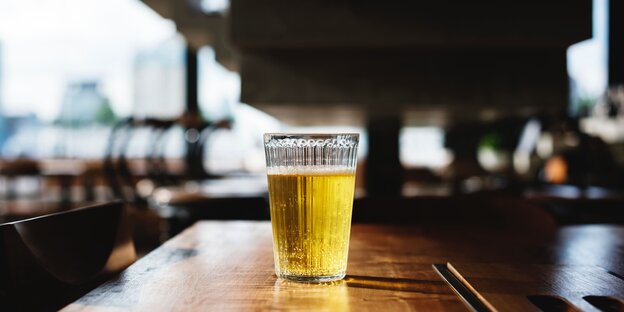 Sonne fällt von hinten durch ein Glas Bier auf einem dunklen Holztisch Sonne fällt von hinten durch ein Glas Bier auf einem dunklen Holztisch