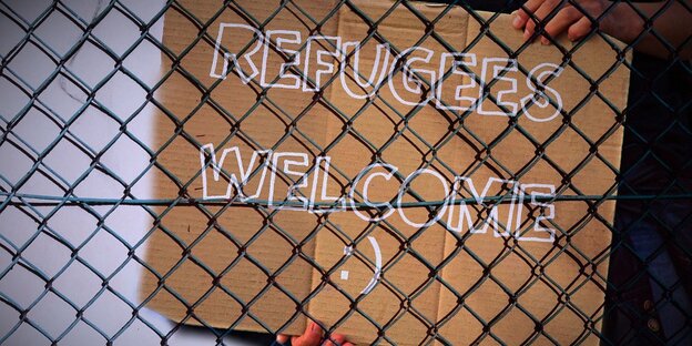 Ein Schild mit „Refugees Welcome“ hinter einem Maschendrahtzaun Ein Schild mit „Refugees Welcome“ hinter einem Maschendrahtzaun