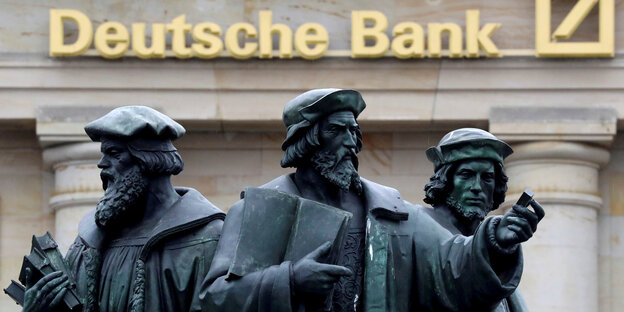 Eine Statue mit drei Männern vor einer Filiale der Deutschen Bank Eine Statue mit drei Männern vor einer Filiale der Deutschen Bank