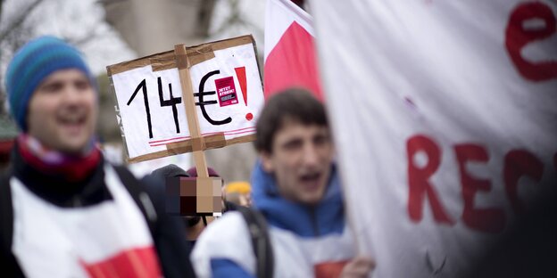 Demonstrierende, einer mit einem Schild auf dem "14 Euro!" steht Demonstrierende, einer mit einem Schild auf dem "14 Euro!" steht