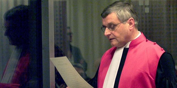 Ein Mann in roter Robe liest von einem Blatt Papier etwas vor Ein Mann in roter Robe liest von einem Blatt Papier etwas vor