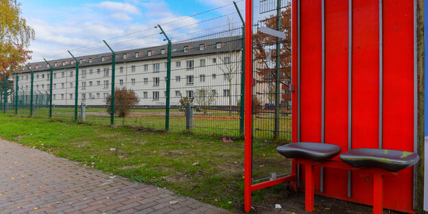 Ein eingezäuntes Kasernengebäude und im Vordergrund ein knallrote Bushaltestelle Ein eingezäuntes Kasernengebäude und im Vordergrund ein knallrote Bushaltestelle