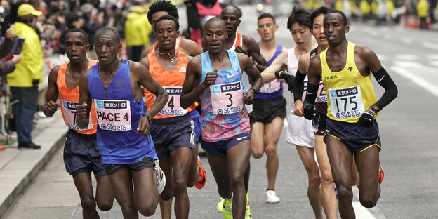 Mehrere Männer in Sportkleidung laufen einen Marathon, am Srraßenrand ist Publikum Mehrere Männer in Sportkleidung laufen einen Marathon, am Srraßenrand ist Publikum