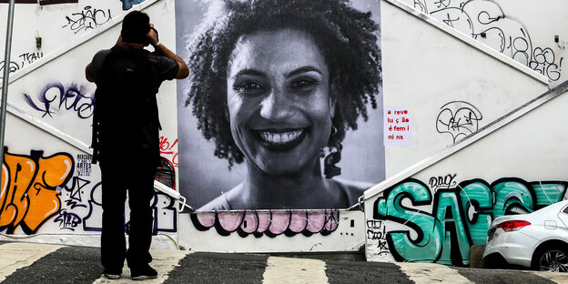 Ein Wandbild mit dem Konterfei von Marielle Franco, davor steht ein Mann und fotografiert Ein Wandbild mit dem Konterfei von Marielle Franco, davor steht ein Mann und fotografiert