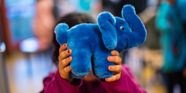 Ein Kind hält einen blauen Elefanten vor sein Gesicht Ein Kind hält einen blauen Elefanten vor sein Gesicht