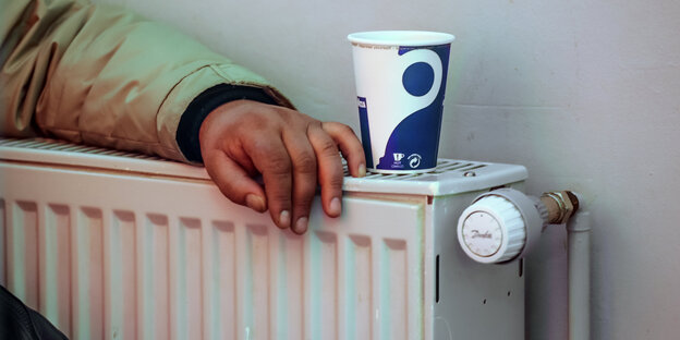 Ein Arm und ein Becher sind auf einer Heizung abgelegt Ein Arm und ein Becher sind auf einer Heizung abgelegt