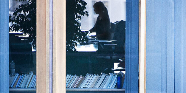 In einem Fenster sieht man den Umriss einer Frau an einem Schreibtisch In einem Fenster sieht man den Umriss einer Frau an einem Schreibtisch