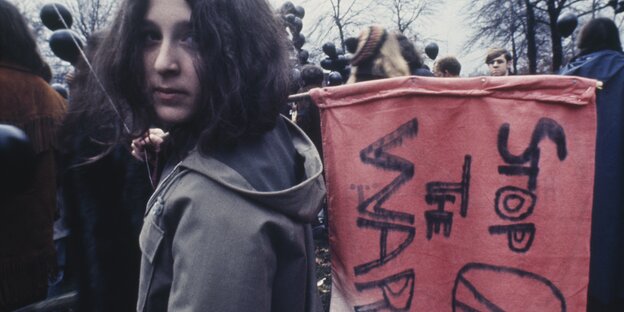 Ein junge Demonstrant hält eine rote Flagge mit der Aufschrift „Stop the War" und dem Peace-Zeichen Ein junge Demonstrant hält eine rote Flagge mit der Aufschrift „Stop the War" und dem Peace-Zeichen