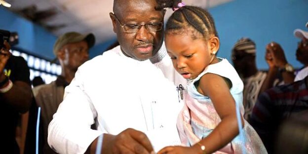 Der Gewinner der Wahlen in Sierra Leone gibt mit einem kleinen Mädchen auf dem Arm seine Stimme in eine Wahlurne ab Der Gewinner der Wahlen in Sierra Leone gibt mit einem kleinen Mädchen auf dem Arm seine Stimme in eine Wahlurne ab