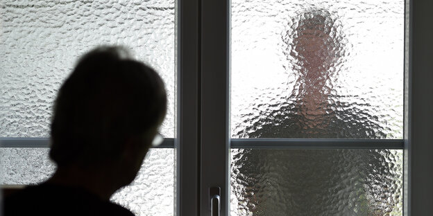 Eine Person nähert sich einer Tür mit Milchglasscheibe hinter der eine andere Person steht. Eine Person nähert sich einer Tür mit Milchglasscheibe hinter der eine andere Person steht.